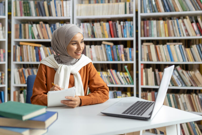 Muslim woman studying with laptop and notebook in library